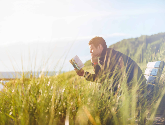 man op bankje in het gras met een boek