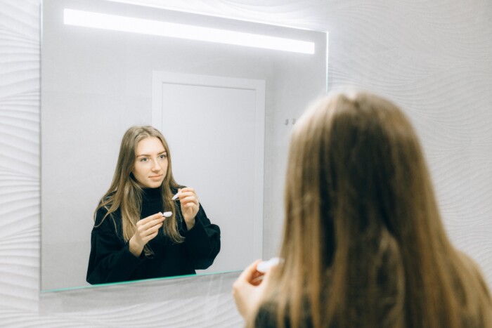 Jonge vrouw die lenzen indoet voor de spiegel